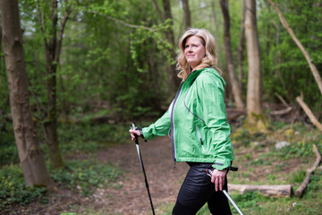 Frau im mittleren Alter draußen in der Natur beim Walken, sie trägt eine grüne Jacke 