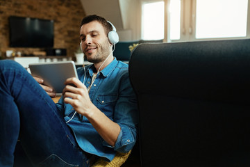 Happy man with headphones watching podcast on touchpad at home.