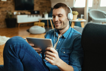 Happy man with headphones surfing the net on digital tablet in the living room.