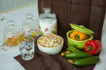 Decorated with lettuce, side view, selective focus . Orange pepper in a green bowl . Water in a glass. Brown tablecloth. Salad with ham, bell pepper, mushrooms, pickles, white sauce, on a white plate.