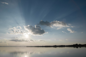 Breathtaking lake landscape at sunset / sun going down and hiding behind clouds / sunlight beams / water reflection