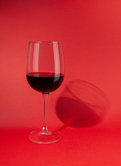 Glass with red wine. On a plain red background. Hard light, sharp shadows. Close-up. Place for text.