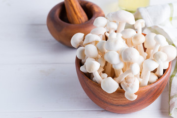 Fresh natural Enoki mushrooms in a wooden bowl made from olive tree on a white wood background.