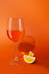 Cocktail aperol spritz. In a glass goblet. Next to the glass are two slices of orange. On a plain orange background. Hard light, sharp shadows. Close-up. Place for text.
