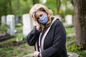 Frau mit Atemmaske auf dem Friedhof, Trauer zur Zeit des Coronavirus 