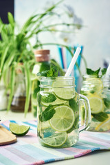 Obraz premium A glass of homemade lemon, lime, and mint lemonade sits on the wooden dining table. Cold, refreshing summer lemonade or mojito.