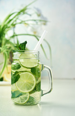 A glass of homemade lemon, lime, and mint lemonade sits on the wooden dining table. Cold, refreshing summer lemonade or mojito.