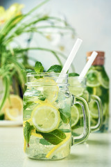 Two glasses and a bottle of homemade lemon, lime, and mint lemonade sit on the wooden dining table. Cold, refreshing summer lemonade or mojito.