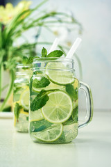 Two glasses of homemade lemon, lime, and mint lemonade sit on the wooden dining table. Cold, refreshing summer lemonade or mojito.