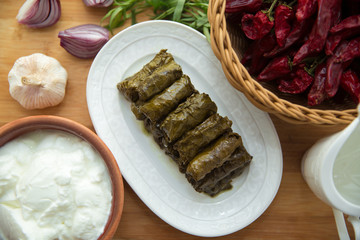 Delicious dolma sarma rice, white yogurt sauce . Garlic, red onion, tarragon . In a stuffed white plate . Yogurt and dried beans in a brown bowl . Red Dry Pepper in Traditional Basket .