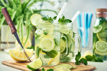 Two glasses and a bottle of homemade lemon, lime, and mint lemonade sit on the wooden dining table. Cold, refreshing summer lemonade or mojito.