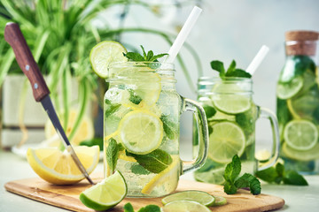 Two glasses and a bottle of homemade lemon, lime, and mint lemonade sit on the wooden dining table. Cold, refreshing summer lemonade or mojito.
