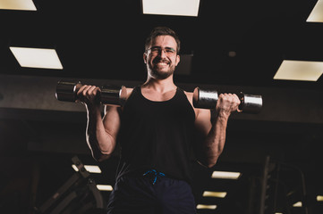 Fototapeta na wymiar A man with an effort does an exercise for biceps and triceps with a dumbbell. Embossed bodybuilder smiles. Muscular guy with glasses in the gym.