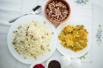 Khan pilaf in a pita . Dry beans on top of pilaf . Dry beans in a brown bowl . Chicken curry on the white plate . red cabbage sauerkraut and black pepper in a small bowl . Shah pilaf on the plate.