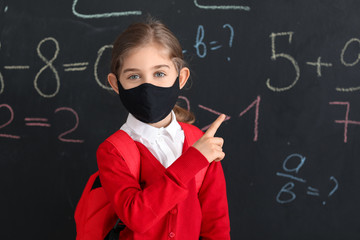 Little girl wearing medical mask near school blackboard