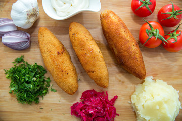Ukrainian tradition food on a wooden board . Red cabbage sauerkraut in a small bowl . mashed potatoes . Mayonnaise, Garlic, Onion, Tomatoes. Chopped coriander.Chicken Kiev cutlets with parsley leaves.