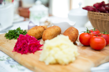 Ukrainian tradition food on a wooden board . Red cabbage sauerkraut in a small bowl . mashed potatoes . Mayonnaise, Garlic, Onion, Tomatoes. Chopped coriander.Chicken Kiev cutlets with parsley leaves.