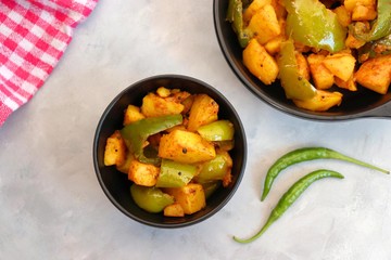 Indian food - Spicy Capsicum and potato stir fried with Indian spices. Aloo and Shimla Mirchi. served in black plate over moody background. 