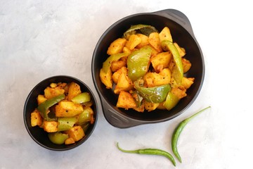 Indian food - Spicy Capsicum and potato stir fried with Indian spices. Aloo and Shimla Mirchi. served in black plate over moody background. 