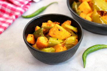 Indian food - Spicy Capsicum and potato stir fried with Indian spices. Aloo and Shimla Mirchi. served in black plate over moody background. 