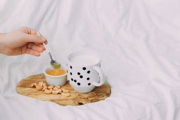 Hot milk in a glass cup and honey on a wooden board. Treatment of hot drink. Treatment of folk remedies in bed. 