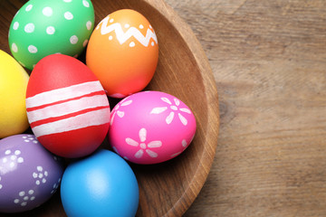 Fototapeta na wymiar Colorful Easter eggs in bowl on wooden background, top view. Space for text