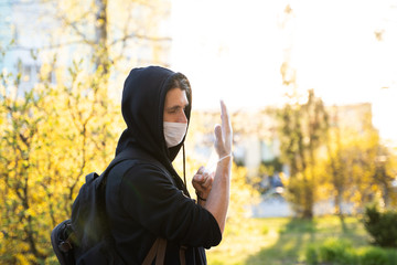 Man in black hoodie in a medical mask wearing rubber gloves to prevent germs, toxic fumes, dust. Prevention of bacterial infection Coronavirus or Covid 19 epidemic on a street. Global quarantine.