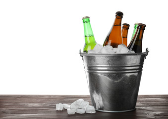 Metal bucket with bottles of beer and ice cubes on wooden table against white background. Space for text