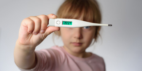 a little girl shows a thermometer with a heat of 39.5. Take care of your loved ones, stay home