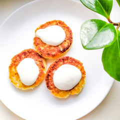 Cheesecake, fresh sour cream. Cheesecakes or cottage cheese pancakes decorated with sour cream on a white plate close-up. Healthy and diet breakfast. Food at home. Cook at home.