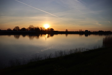 Fototapeta na wymiar The sun rises over the water of the river Hollandsche IJssel near the dike at Park Hitland