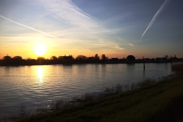 The sun rises over the water of the river Hollandsche IJssel near the dike at Park Hitland