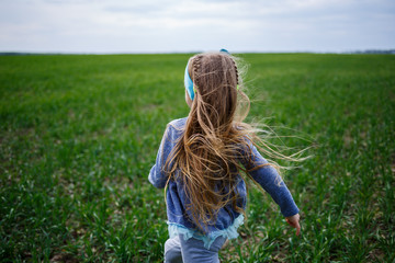 Fototapeta premium little girl child runs on green grass in the field, sunny spring weather, smile and joy of the child, blue sky with clouds