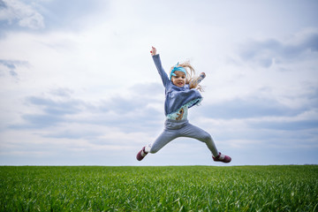 little girl child runs and jumps, green grass in the field, sunny spring weather, smile and joy of the child, blue sky with clouds