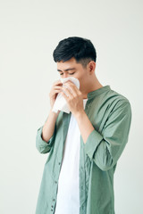 Young asian man sneezing after get allergy or flu virus and using tissue paper for swipe on nose at...