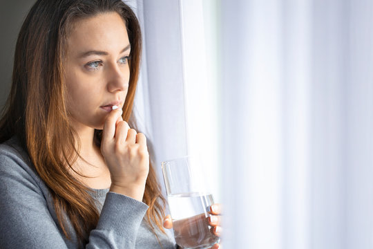 Young Sadness Woman Putting White Pill In Mouth