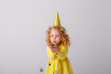 little girl blonde in a yellow dress catches confeti smiling happy on white background