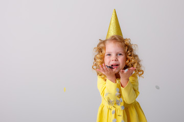 little girl blonde in a yellow dress catches confeti smiling happy on white background