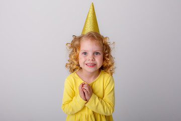 a little girl a blonde in a yellow dress with a hat asks for a birthday folded her hands in supplication on a white background