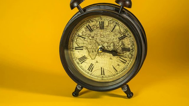 Antique alarm clock with world map running time lapse 4k on yellow background studio 
