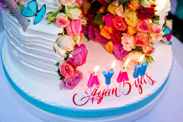 Two-layer cake . Wedding cake decorated with colorfull roses. Celebration party concept. flowers in the middle of the place where the cake is cut on the blue butterfly . White cake with rounded .