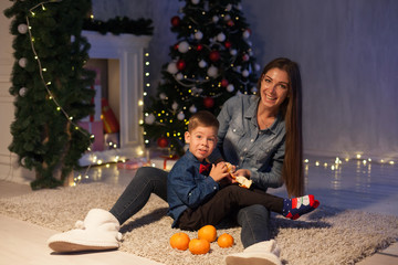 Beautiful mom with son at christmas tree with new year decor gifts