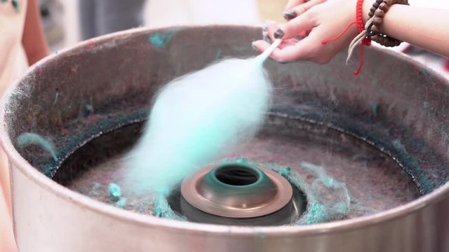 Closeup of vendor's hands twirl a stick in cotton candy making machine to make blue cotton candy at street food stall in local market 