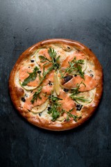 Italian pizza with cheese salmon arugula on black background top