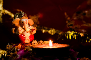 low light photography little staue of ganesha with terracotta lamp on flower petals against blurry...