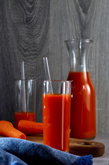 Two glasses of freshly squeezed carrot juice with tubes and a carafe of juice on the background of a cutting Board and a kitchen towel. Natural vitamins and minerals. Vertical.