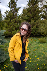 Young woman in the park in spring. Curly brunette in a yellow jacket