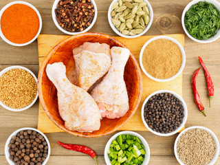 Raw chicken drumsticks in a bamboo bowl and spice set: red chili pepper, masala, black pepper, cumin, fenugreek, cloves, green onion, fennel. Healthy eating concept