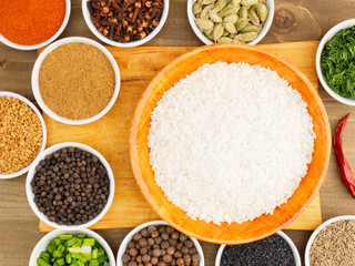 Raw white round grain rice in a bamboo bowl and spice set: red chili pepper, masala, black pepper, cumin, fenugreek, cloves, green onion, fennel