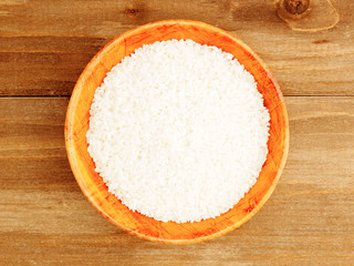 Raw white round grain rice in a bamboo bowl on a brown wooden background